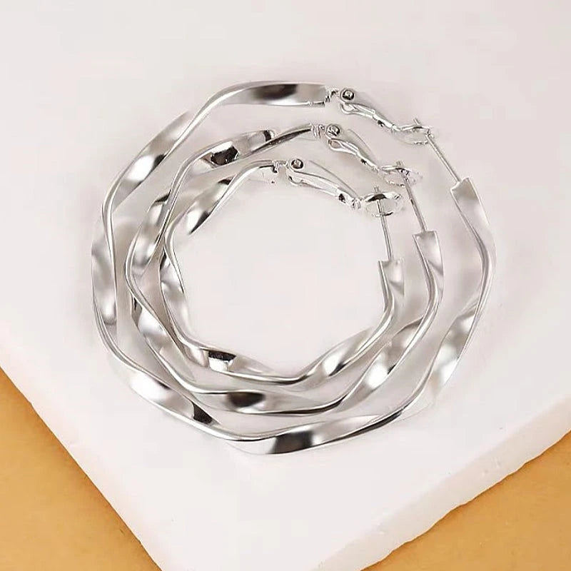 Three sizes of silver twisted wavy hoop earrings flat lay display
