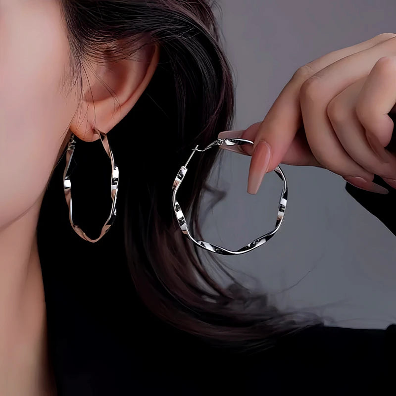 Silver twisted irregular hoop earrings, one worn on ear, trendy fashion statement jewelry