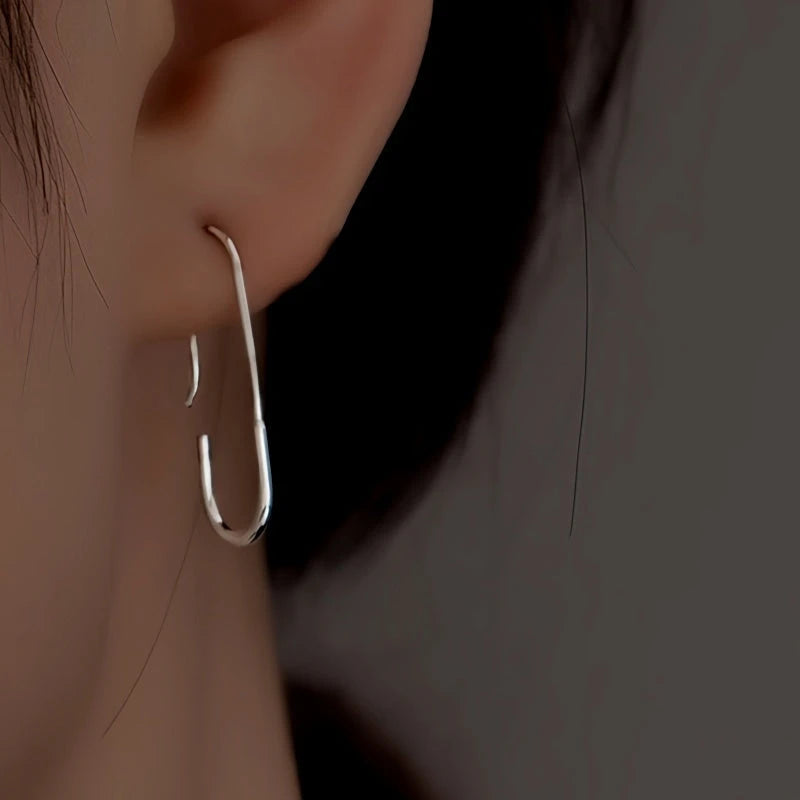 Silver minimalist paperclip-shaped earring worn on ear, close-up