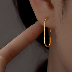Gold minimalist paperclip drop earring worn on ear, close-up