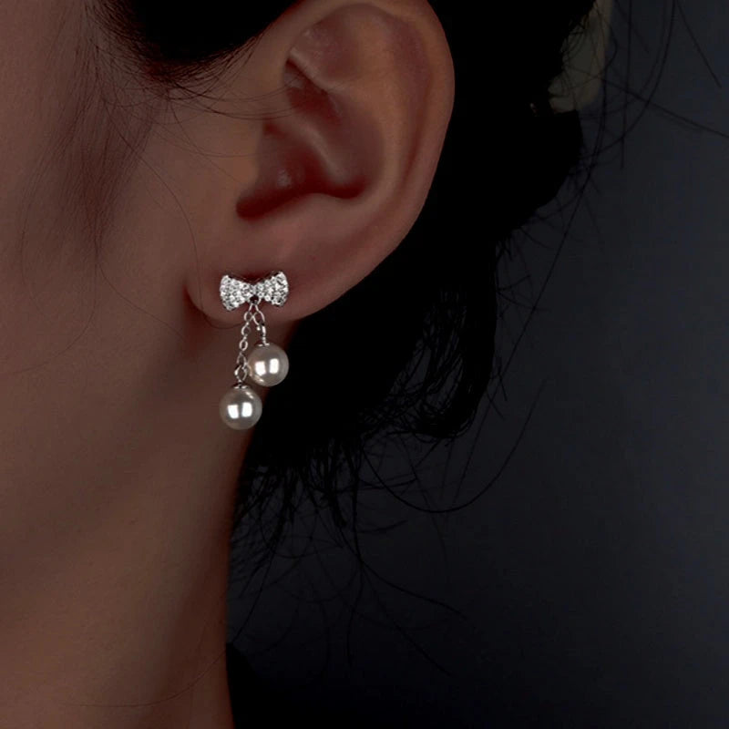 Model showcasing the dangle and style of the Sterling Silver Zircon Diamond Bow Pearl Tassel Earrings