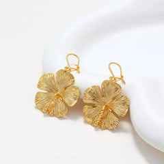 Gold hibiscus flower drop earrings styled with white curved display prop