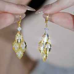 Pair of gold leaf cubic zirconia dangle earrings held by manicured fingers
