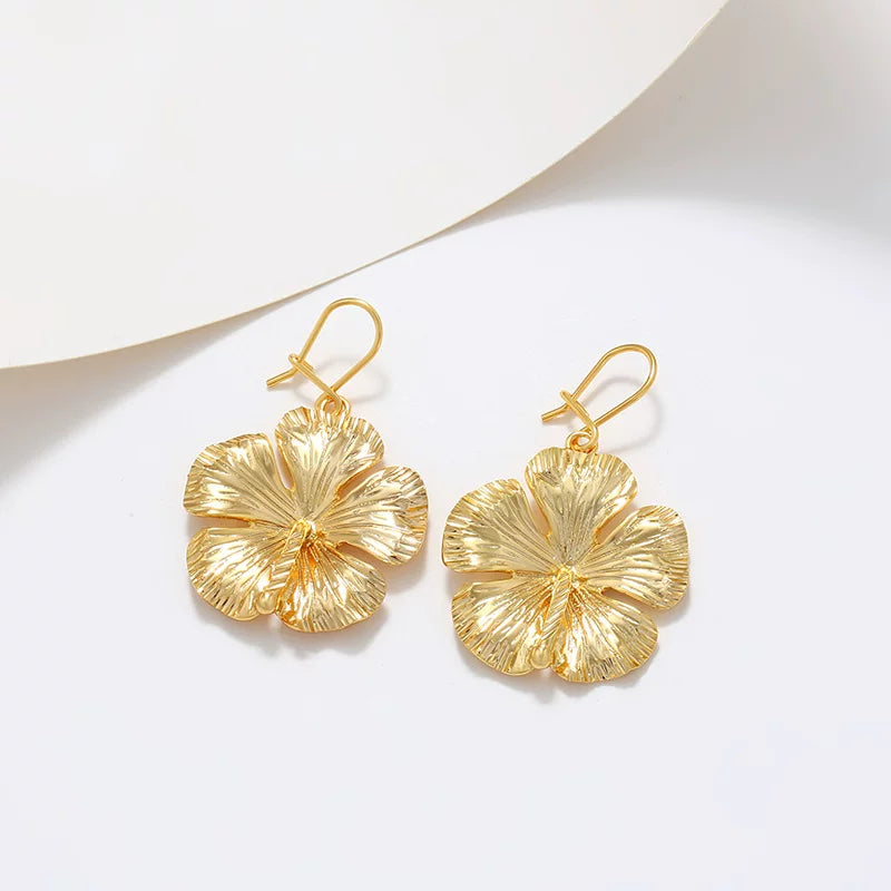 Gold hibiscus floral drop earrings on curved white minimalist background