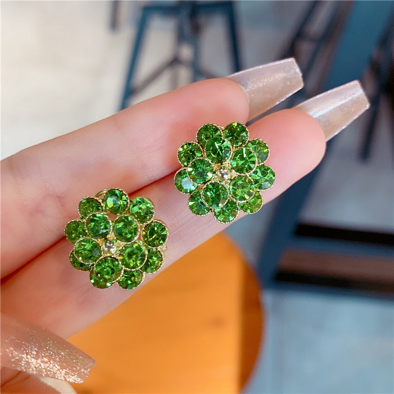 Green rhinestone flower stud earrings held on a finger