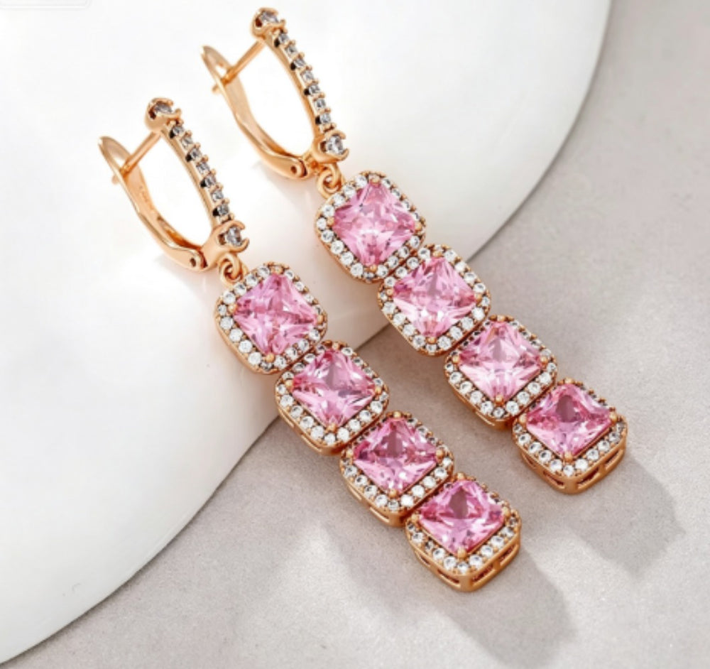 Rose gold pink cushion cut halo drop earrings, angled styled view on white decor surface
