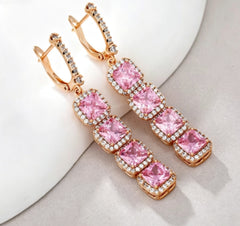 Rose gold pink cushion cut halo drop earrings, angled styled view on white decor surface