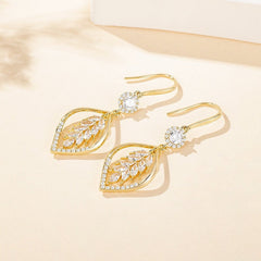 Pair of gold leaf design CZ drop earrings laid flat on warm beige surface